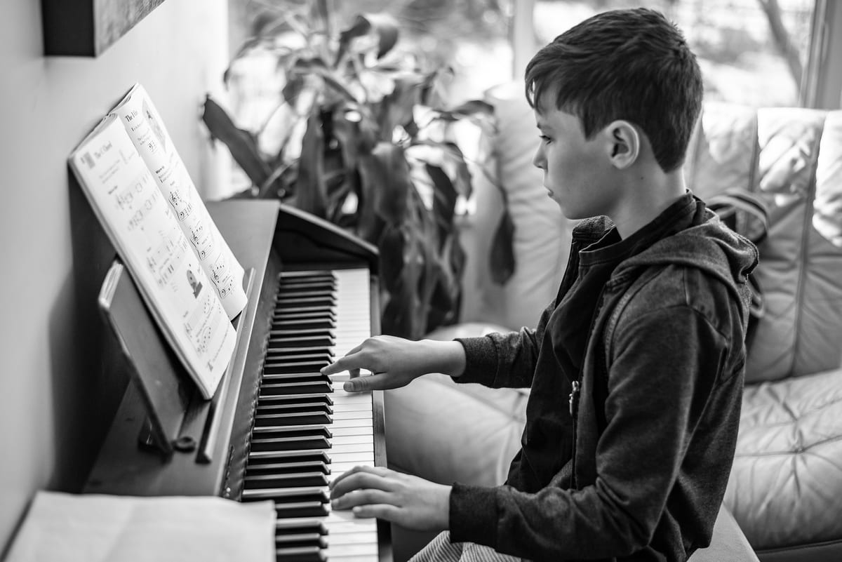 A student practicing piano during a lesson, sheet music propped on the rest.